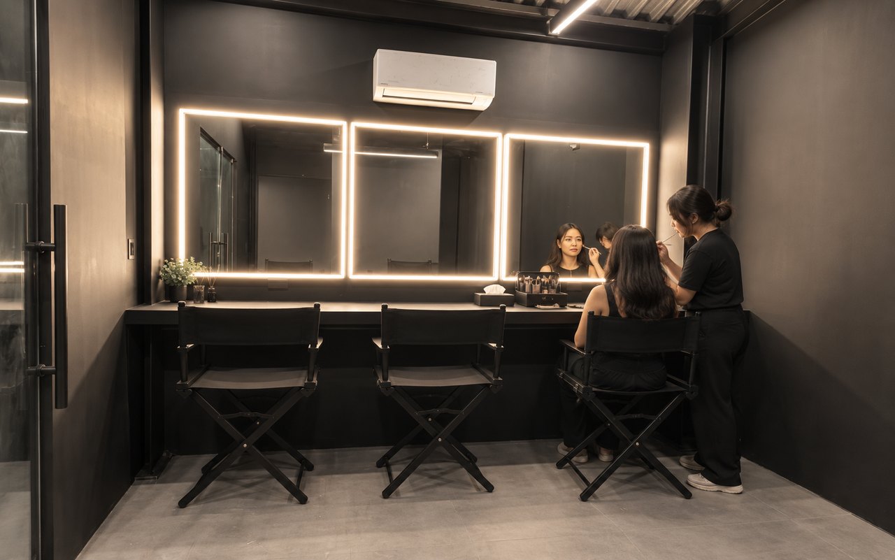 AI-staged visualization based on Studio W9 room photographs, showing the compact dressing room with three illuminated vanity mirrors, a centered split air conditioner and a makeup preparation setup.